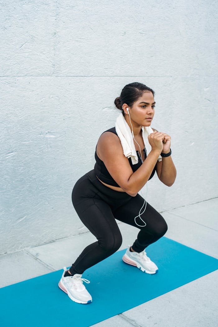 Athletic woman in sportswear doing squats on yoga mat. Outdoor fitness training.
